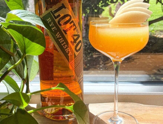 Cocktail with a stone fruit garnish sitting next to a bottle of Lot 40 whiskey.