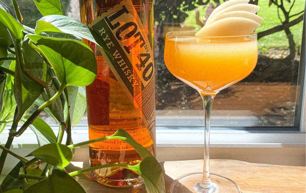 Cocktail with a stone fruit garnish sitting next to a bottle of Lot 40 whiskey.