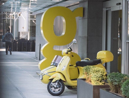Large yellow 'g' sculpture with a yellow vespa parked in front of it.
