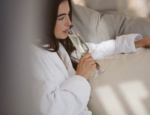 A woman in a white Fairmont robe drink a glass of champagne.