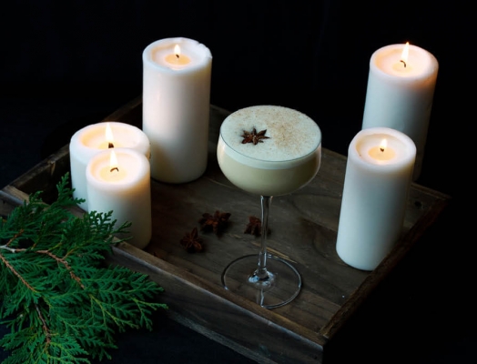 Eggnog in a cocktail glass surrounded by candles.