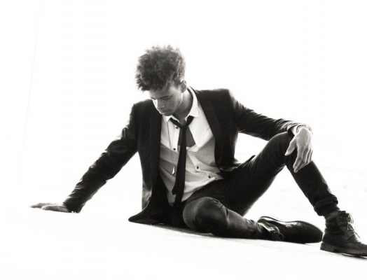 A black and white iamge of Zach Person sitting on the ground in front of a white backdrop