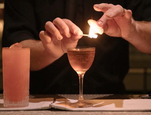 A cocktail glass with a match lit torching a garnish